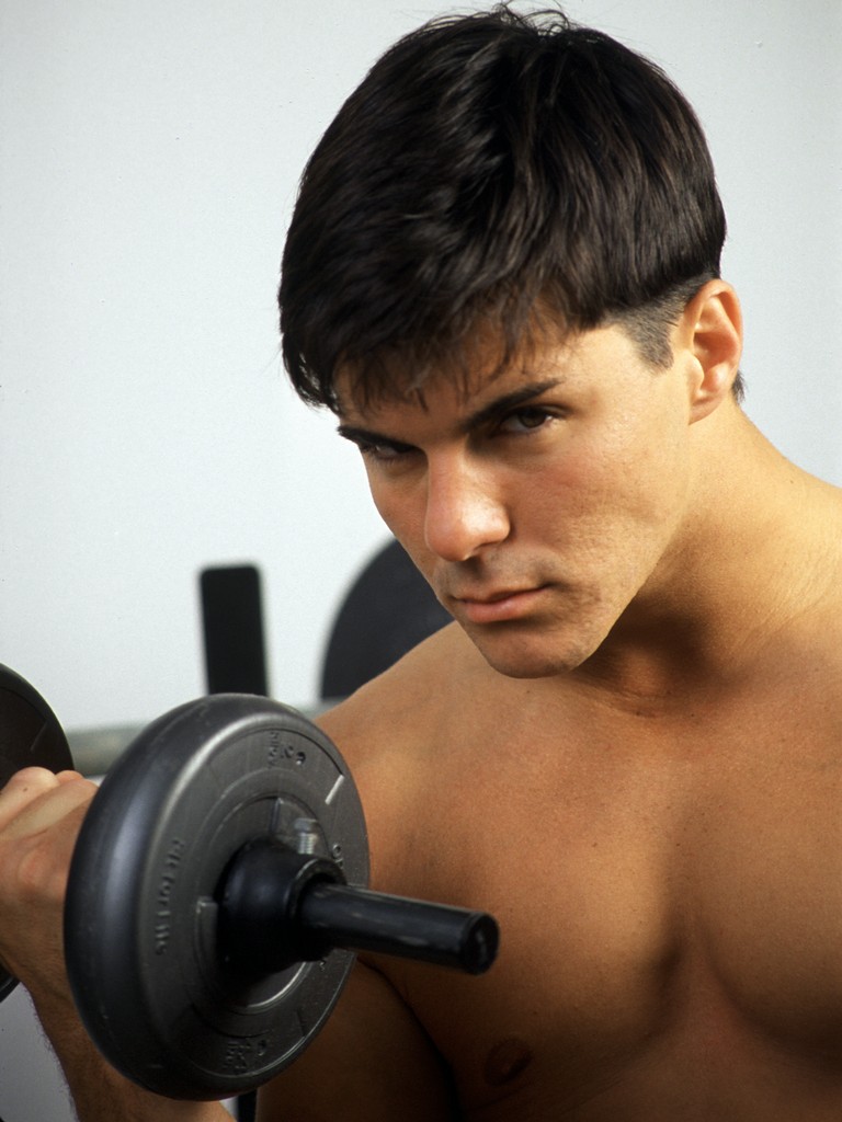 90s pornstar DCOTA poses nude indoors with weights.