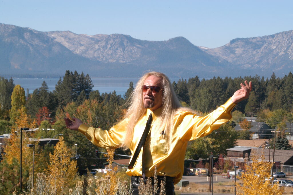 Daddy Tiger arms spread wide in front of Lake Tahoe in a shiny satin shirt.